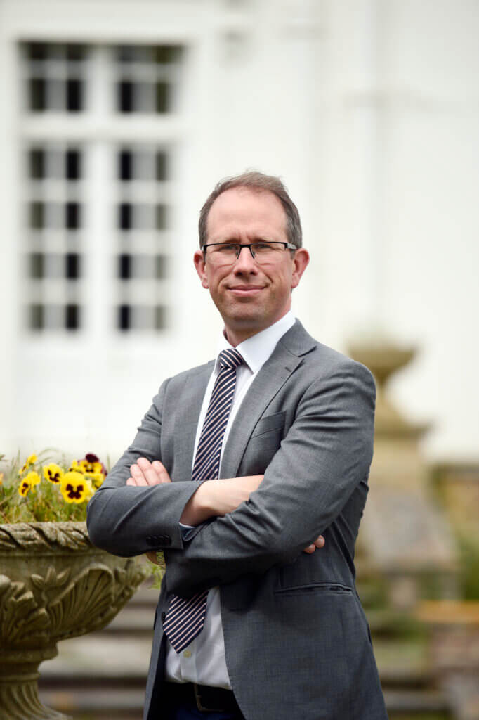 Police and Crime Commissioner, Matthew Barber, stood outside building and next to flower arrangement with arms crossed